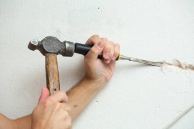 Binanın tamiri. Bir adam duvara kablo döşemek için hendek kazar. Duvara elektrik kabloları döşeniyor.