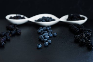 Siyah bir masada beyaz bir tabakta farklı türde siyah böğürtlen. Şık mevsimlik vitaminler.