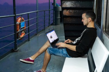 Genç bir adam bir geminin güvertesinde dizüstü bilgisayarda çalışıyor. Uzaktan kumanda. Hep görüşüyoruz.