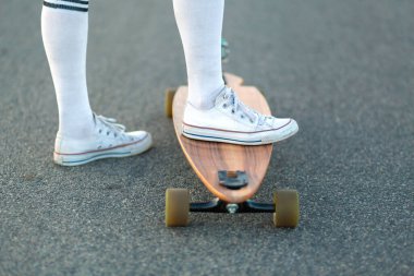 Aşırı komik bir şekilde dinlenen beyaz ayakkabılı bayanın bacağını kapat. Tahta kaykayına bin. Modern şehirli hippi kız eğleniyor. Kaykay yapmak için güneşli bir yaz günü ve iyi eğlenceler..