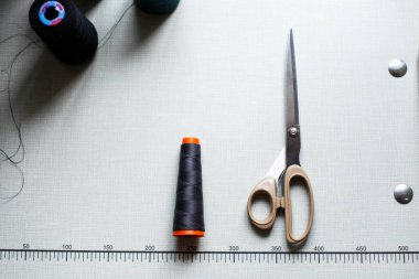 Üzerinde işaretler olan beyaz bir masanın üstündeki makas ve ipliğin en üst görüntüsü. Dikiş endüstrisi. Giysi imalatı.