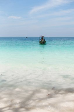 Temiz kumlu bir sahilden mavi göldeki bir tekneye.