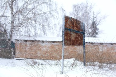 Karla kaplı kırmızı tuğlalı bir binanın arka planındaki paslı yol tabelası..