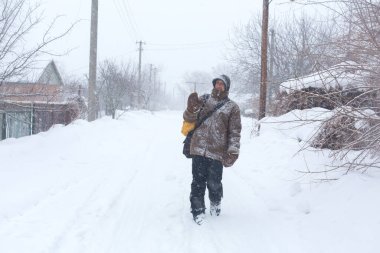 Kırsal bir adam kışın sarı bir sırt çantasıyla sokakta yürüyor. Kar fırtınası.