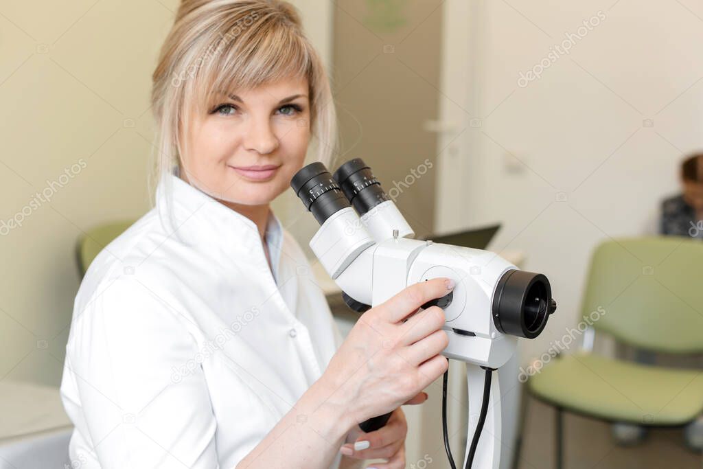 Portrait of a smiling female blond doctor gynecologist near colposcope. Examination by a gynecologist. Female health concept.