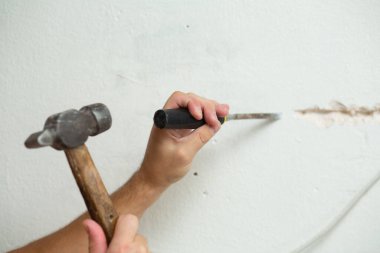 Binanın tamiri. Bir adam duvara kablo döşemek için hendek kazar. Duvara elektrik kabloları döşeniyor.