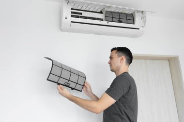 Adam evdeki klimanın filtresini tozdan temizliyor. Çok kirli bir klima filtresi. İklim ekipmanı bakımı