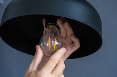 Yakın plan. Bir el şık bir çatı katı lambasında ampulü değiştirir. Spiral filament lamba. Modern iç dekorasyon