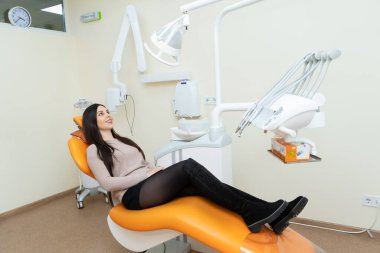 Kız hasta dişçide bir sandalyede doktor bekliyor.