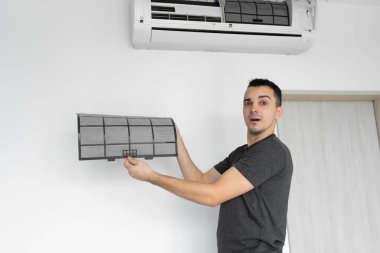 Adam evdeki klimanın filtresini tozdan temizliyor. Çok kirli bir klima filtresi. İklim ekipmanı bakımı