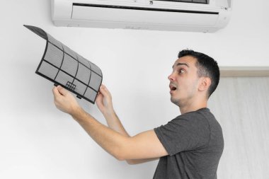 Adam evdeki klimanın filtresini tozdan temizliyor. Çok kirli bir klima filtresi. İklim ekipmanı bakımı