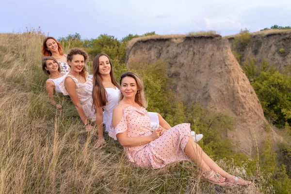 A cheerful company of beautiful girls friends enjoy a picturesque panorama of the green hills at sunset.