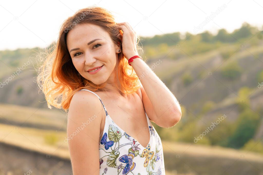 Beautiful red-haired girl is having fun and dancing in a field at sunset.