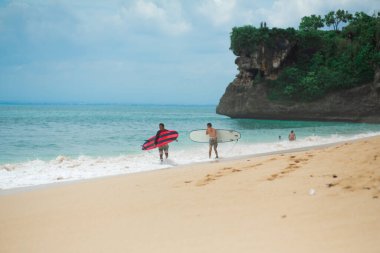 Sörfçü. Sörf tahtası olan sörfçü adam kumsalda yürüyor. Sağlıklı yaşam tarzı, su aktiviteleri, Su Sporu. Güzel Okyanus. Bali, Endonezya - 03 / 24 / 2018