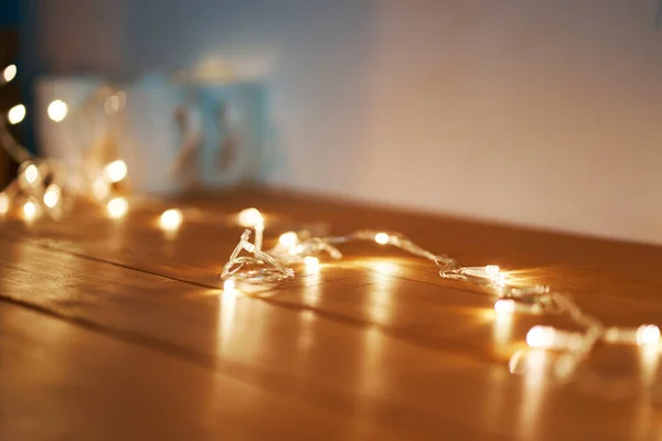 Garland glowing with warm light on the wooden floor. The atmosphere of the Christmas holidays