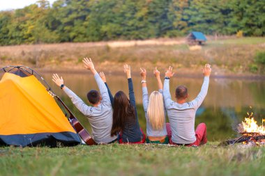 Arkadan ateş et. Nehir kenarında kamp yapan bir grup mutlu arkadaş el ele tutuşup manzaranın tadını çıkarıyorlar. Tatil eğlencesi.