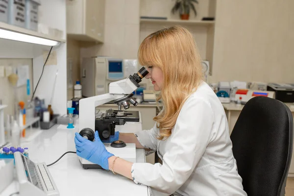 顕微鏡を通して見る赤い髪の女性研究室の技術者は血液を分析 — ストック写真