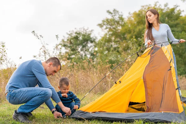 Happy family with little son set up camping tent. Happy childhood, camping trip with parents. A child helps to set up a tent.