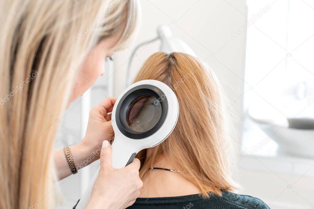 A trichologist examines the condition of the hair on the patients head with a dermatoscope. In a bright cosmetology room.