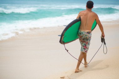 Sörfçü. Sörf tahtası olan sörfçü adam kumsalda yürüyor. Sağlıklı yaşam tarzı, su aktiviteleri, Su Sporu. Güzel Okyanus
