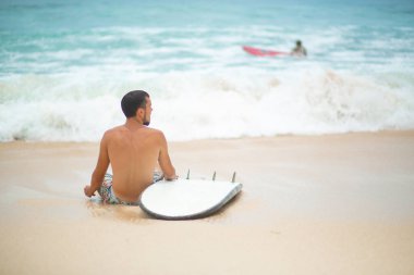 Adam sörf yaptıktan sonra kumlu bir tropik plajda dinleniyor. Yaz mesleğinde sağlıklı aktif yaşam tarzı.