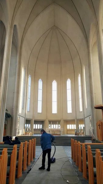 Bir kadın kilise salonundaki halıyı süpürüyor. İzlanda - 01.17.2018