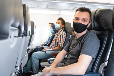 Uçak yolcuları yüzlerine tıbbi maske takıyorlar. Koronavirüs salgını sırasında hava yolculuğu. Havayolu gereksinimleri