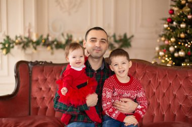 Mutlu baba Noel ağacının yanındaki kanepede oğullarına sarılıyor. Sıcak aile ortamı. Sevgi dolu kucaklaşmalar, tatilciler. Birliktelik kavramı.