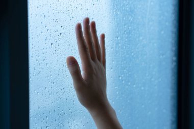 Yağmur sırasında kadın eli pencerede. Su damlalarında cam.