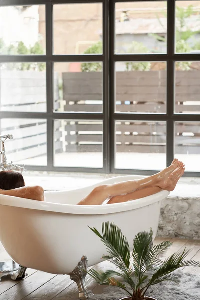 一个漂亮的女人在一个白色的浴缸里 在一个明亮的房间里 一个大窗户里 玩得很开心 — 图库照片