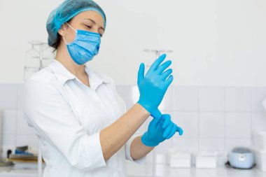 Beyaz önlüklü bir hemşire, tıbbi bir işlemden önce parlak bir çalışma odasında lastik eldiven giyer.