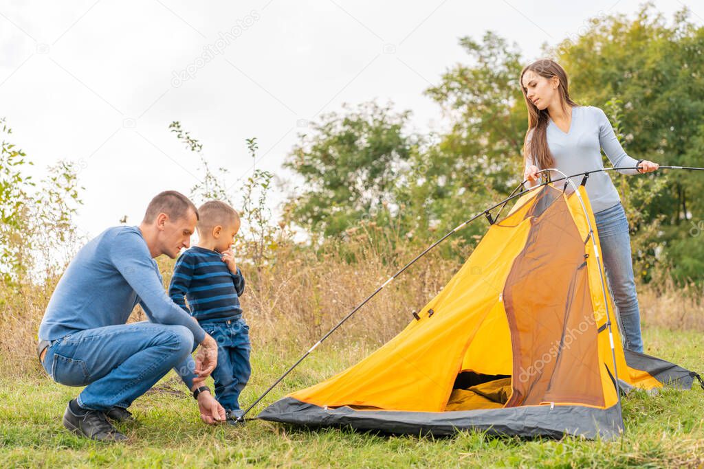 Happy family with little son set up camping tent. Happy childhood, camping trip with parents. A child helps to set up a tent.