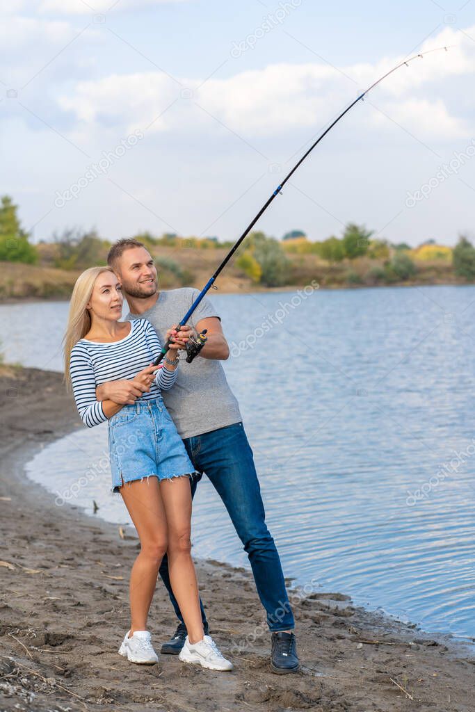 Happy young couple fishing by blue lakeside.