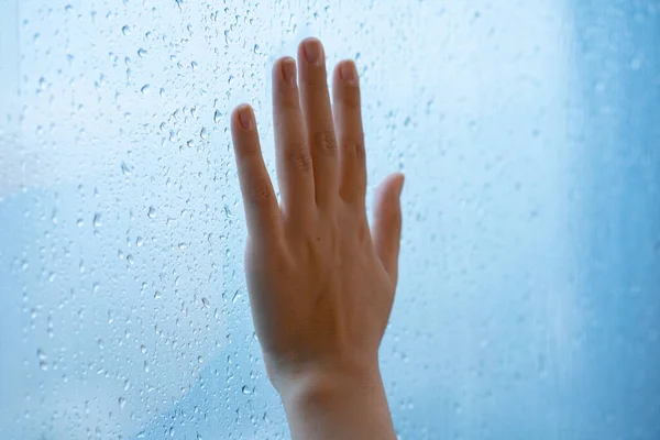 Female hand at the window during the rain. Glass in drops of water