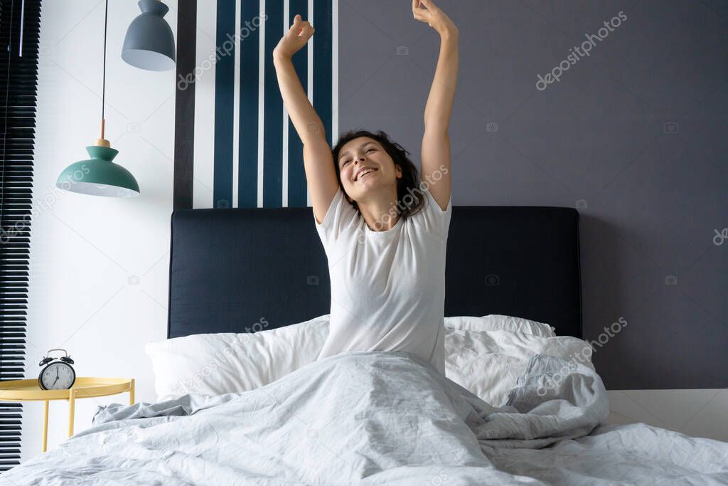 Beautiful girl wakes up in a good mood in a stylish apartment. Stretches with a smile starting the day.