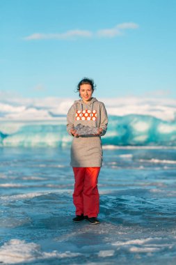 Bir kız, kışın İzlanda 'da bir buzulun yanında dururken elinde şeffaf bir buz parçası tutuyor..