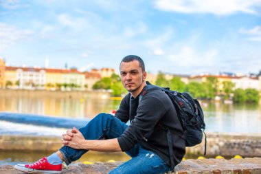 Sırt çantalı bir turist Prag 'da, Vltava nehrine bakan setin kenarında oturuyor..