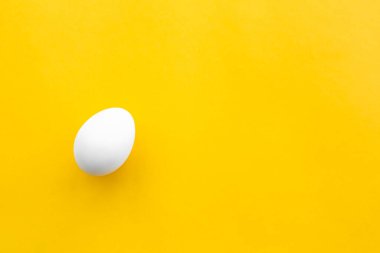 Sarı arka planda beyaz bir tavuk yumurtası var. Sağlıklı organik gıda ve diyet konsepti. Paskalya teması.