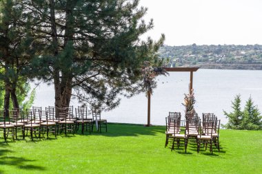 Açık hava düğün töreni için güzel bir mekan. Düğün kemeri ve nehir manzaralı yeşil çimenlikte konuk sandalyeler.