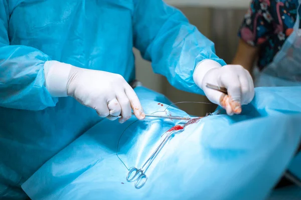 一名戴口罩的男性外科医生在手术室里与一名助理和一名麻醉师一起工作 这个手术由医疗队负责 手套手拿着一个无关紧要的计划 浅蓝色的 — 图库照片