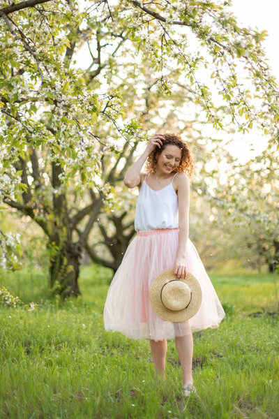 Young attractive woman with curly hair walking in a green flowered garden. Spring mood.