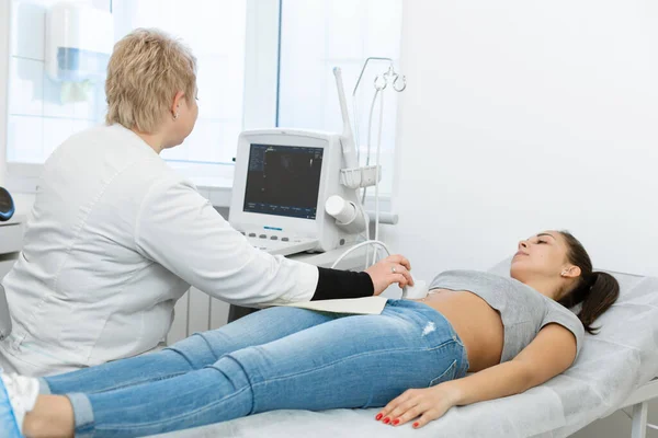 The doctor conducts an ultrasound diagnosis of the patients abdomen and internal organs. A girl lies on a couch in an ultrasound diagnostic room.