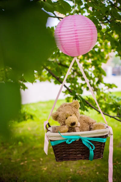 street decorations for a children\'s party. A basket with a teddy bear in a air balloon in a green park.