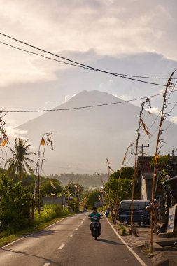 Köyde tatil için dekore edilmiş yol volkanının manzarası. Yol boyunca bambu süslemeleri. Gün batımından önce Agung Dağı 'nın bulutlarla kaplı bir manzarası. Bali, Endonezya - 10.12.2022