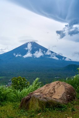 Büyük taşlı bir bakış açısı ve Bali adasındaki yağmurlu bir günde Agung 'un bulutlarla kaplı kutsal volkanı. Dağın manzarası