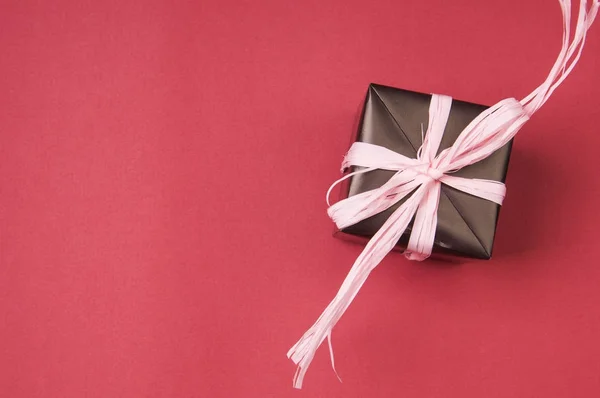 Caixa de presente com laço rosa no fundo vermelho — Fotografia de Stock