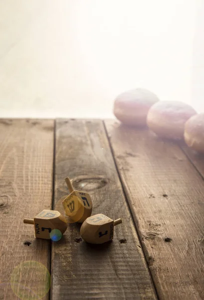 Still life for jewish holiday Hanukkah with 3 donuts and 3 dreidels on wooden rustic table.Hanukkah celebration concept.Lens Fleur copy space. Focus on the Deidls.copy space