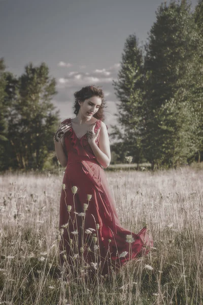 穿着红色连衣裙的成年妇女在草地上摆姿势 — 图库照片