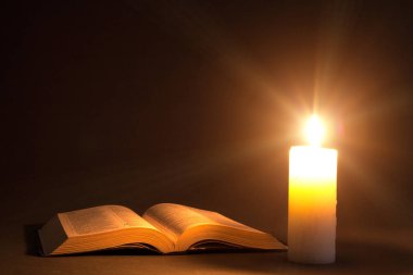 a bible on the table in the light of a candle clipart