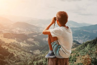 gün batımında yaz dağlarında kütük üzerinde duran ve doğanın manzarasının keyfini çıkaran bir çocuk